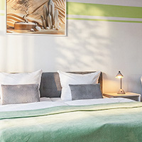 Hell eingerichtetes Schlafzimmer mit zwei Betten, Kissen und einer kleinen Nachttischlampe.