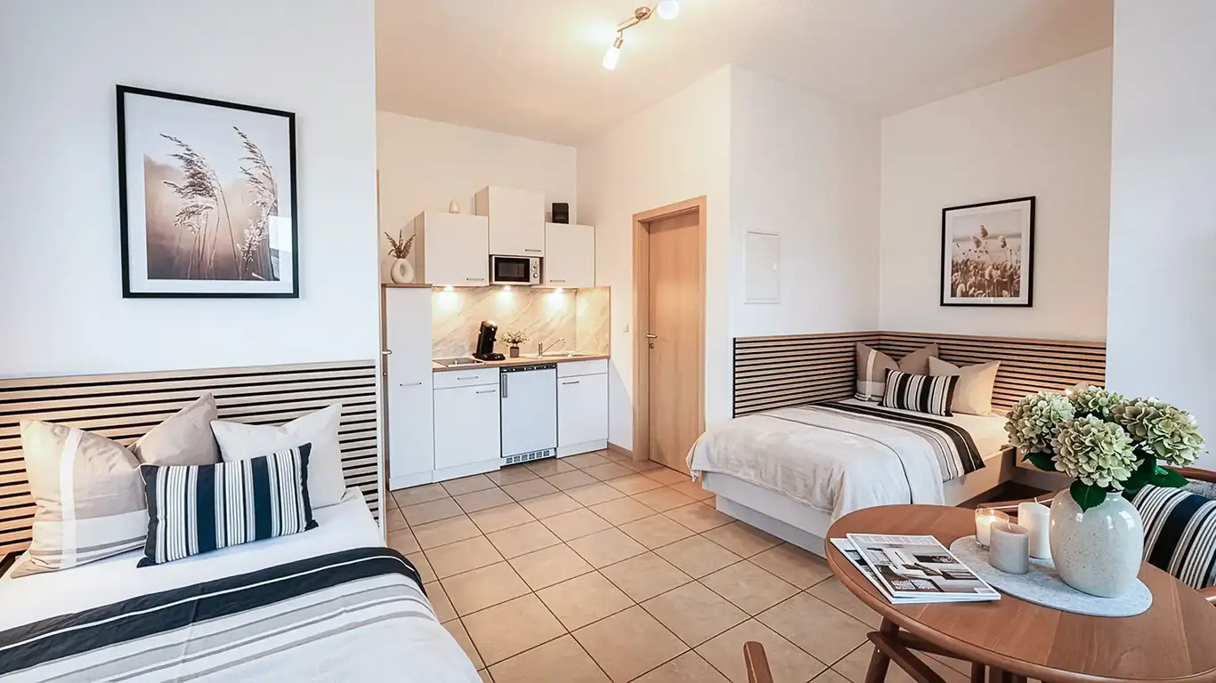 Modernes Studio mit zwei Einzelbetten, kleiner Küchenzeile, Holztisch mit Blumen und Kerzen in Vase.