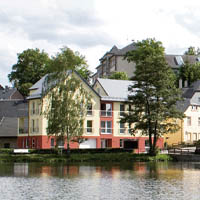 Mehrstöckiges Wohngebäude in Gelb und Weiß an einem ruhigen See, umgeben von Bäumen.