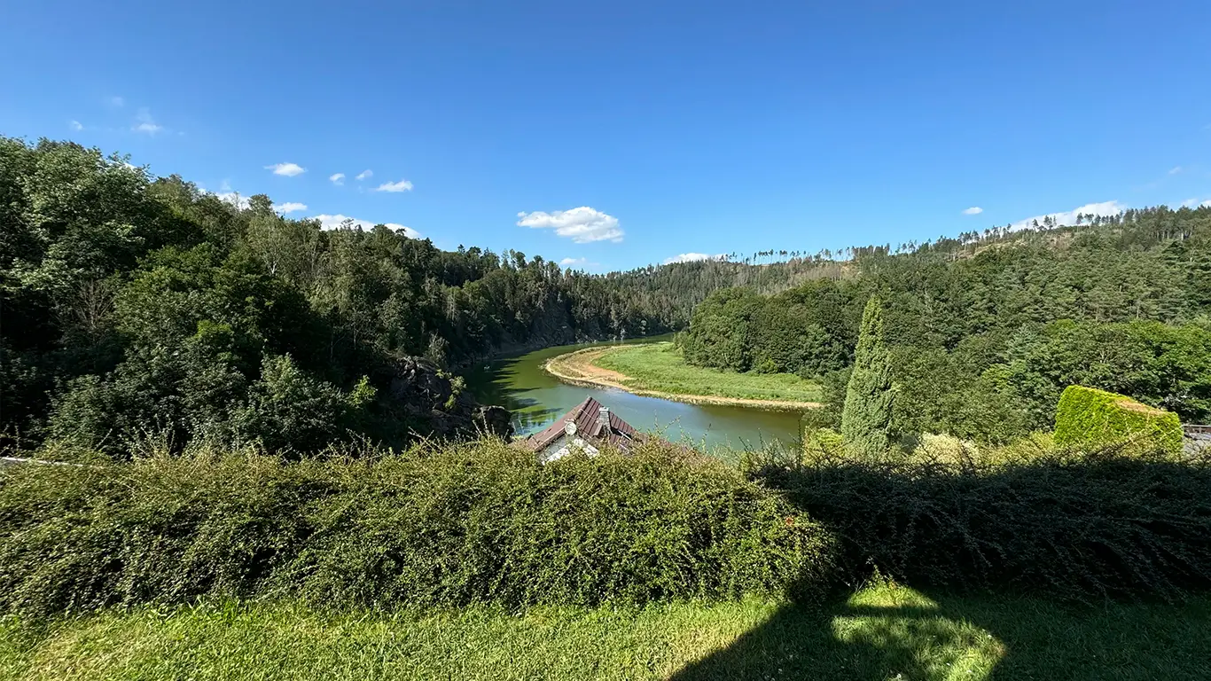 Blick auf einen Fluss, der von dicht bewaldeten Hügeln umgeben ist, unter einem klaren blauen Himmel.