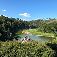 Blick auf einen Fluss, der sich durch eine grüne, bewaldete Landschaft unter blauem Himmel schlängelt.
