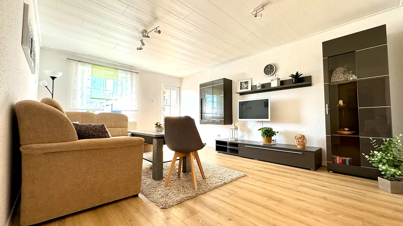 Helles Wohnzimmer mit braunem Sofa, grauem Stuhl, Teppich, modernem Holzfußboden und Wandregalen mit Fernseher.