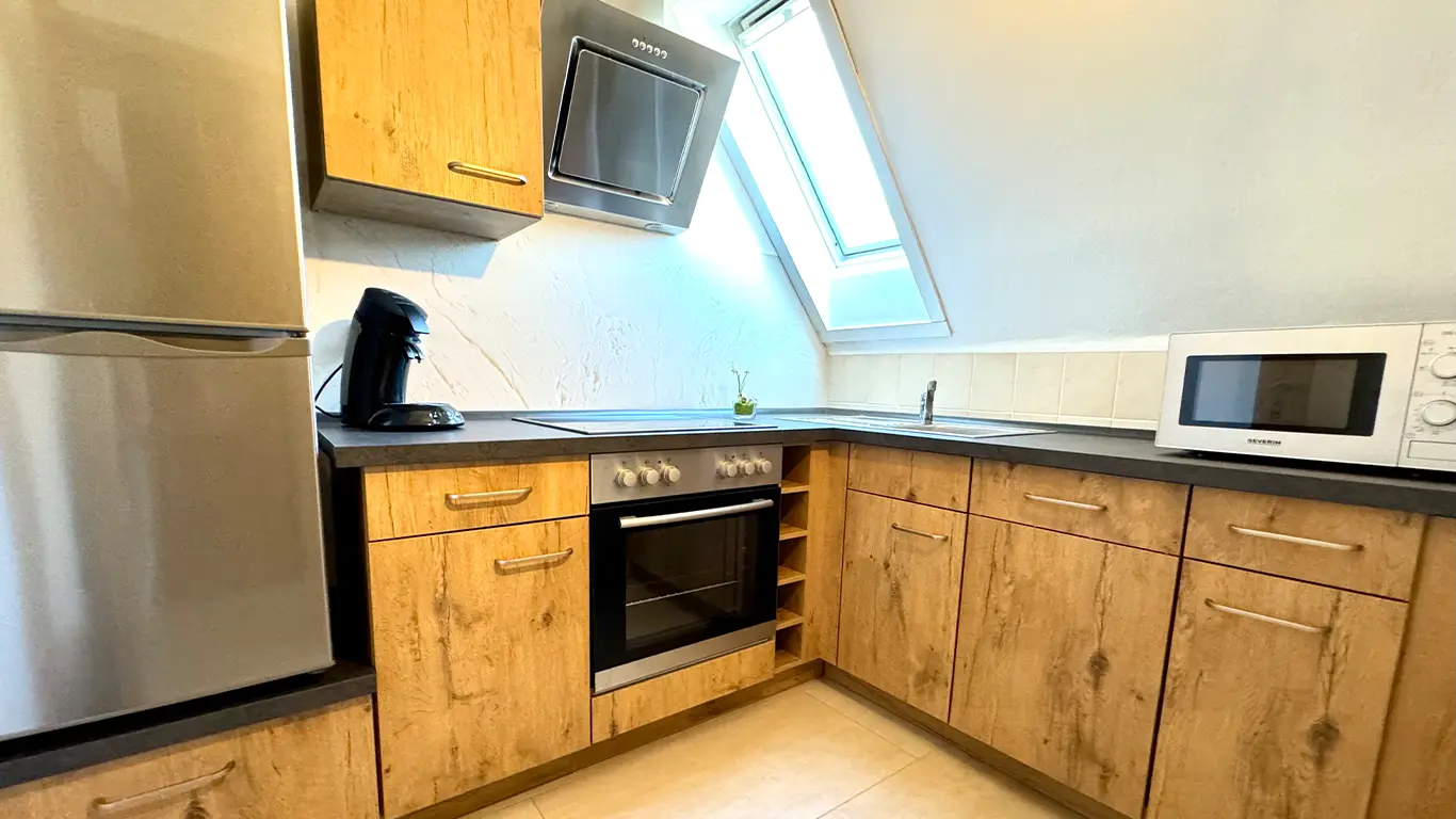 Moderne Küche mit Holzmöbeln, Edelstahl-Kühlschrank, eingebautem Ofen, Kaffeemaschine, Mikrowelle und Dachfenster.