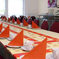 Ein festlich gedeckter Tisch mit orangenen Stoffservietten, weißen Tassen und einem gelben Tischläufer mit Blumendesign.